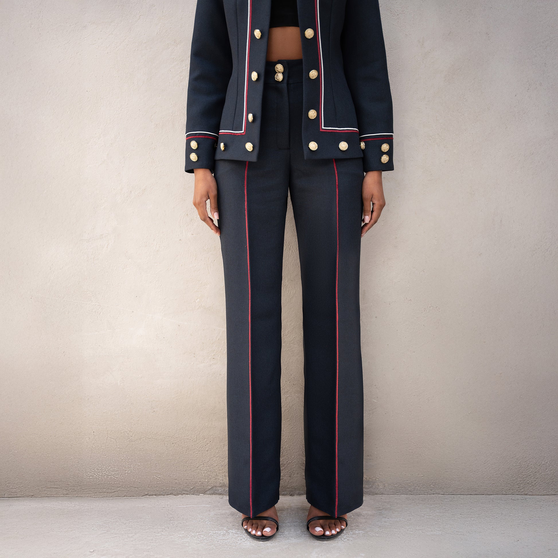 Detailed view of the Frame trousers and jacket hem, showing vertical red lines and golden button embellishments.