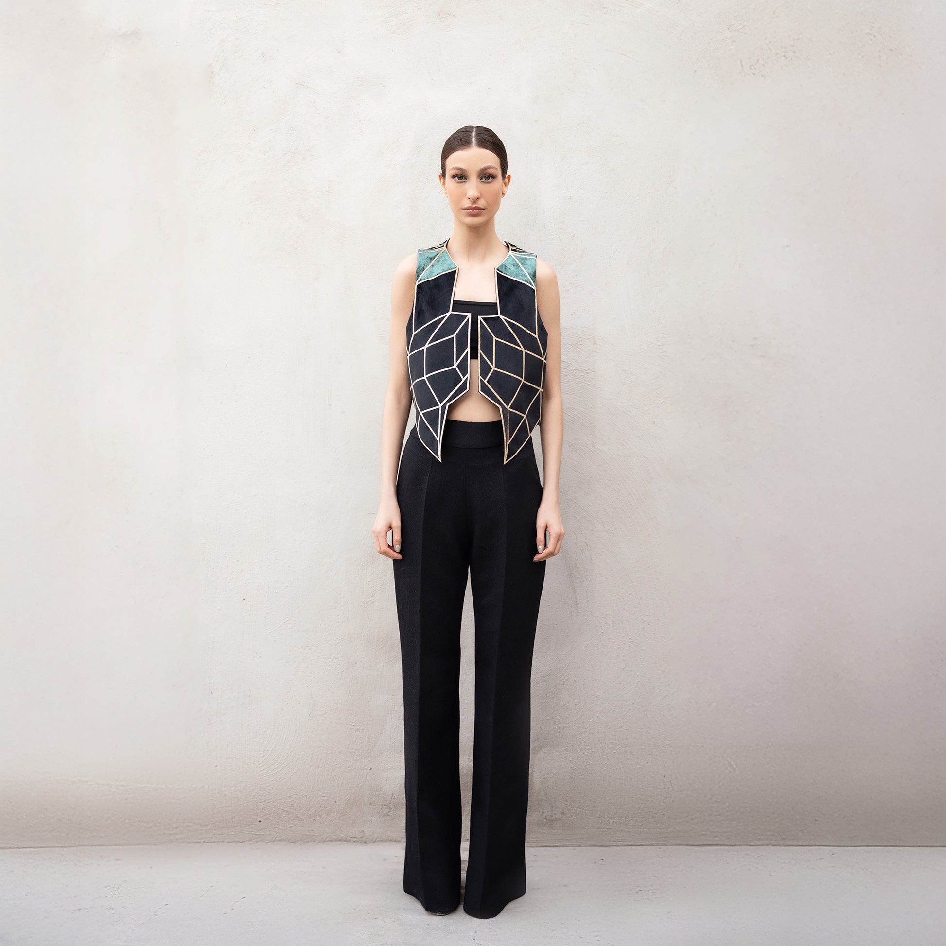 A woman wearing a sleeveless velvet vest with golden laser-cut geometric patterns inspired by the Panther Facade, featuring green velvet shoulder panels and paired with black wide-leg trousers.