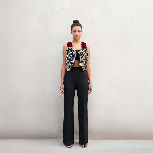 A woman wearing a sleeveless vest made of premium velvet with golden laser-cut geometric patterns inspired by Chehel Panjereh in Isfahan, paired with high-waisted black wide-leg trousers.